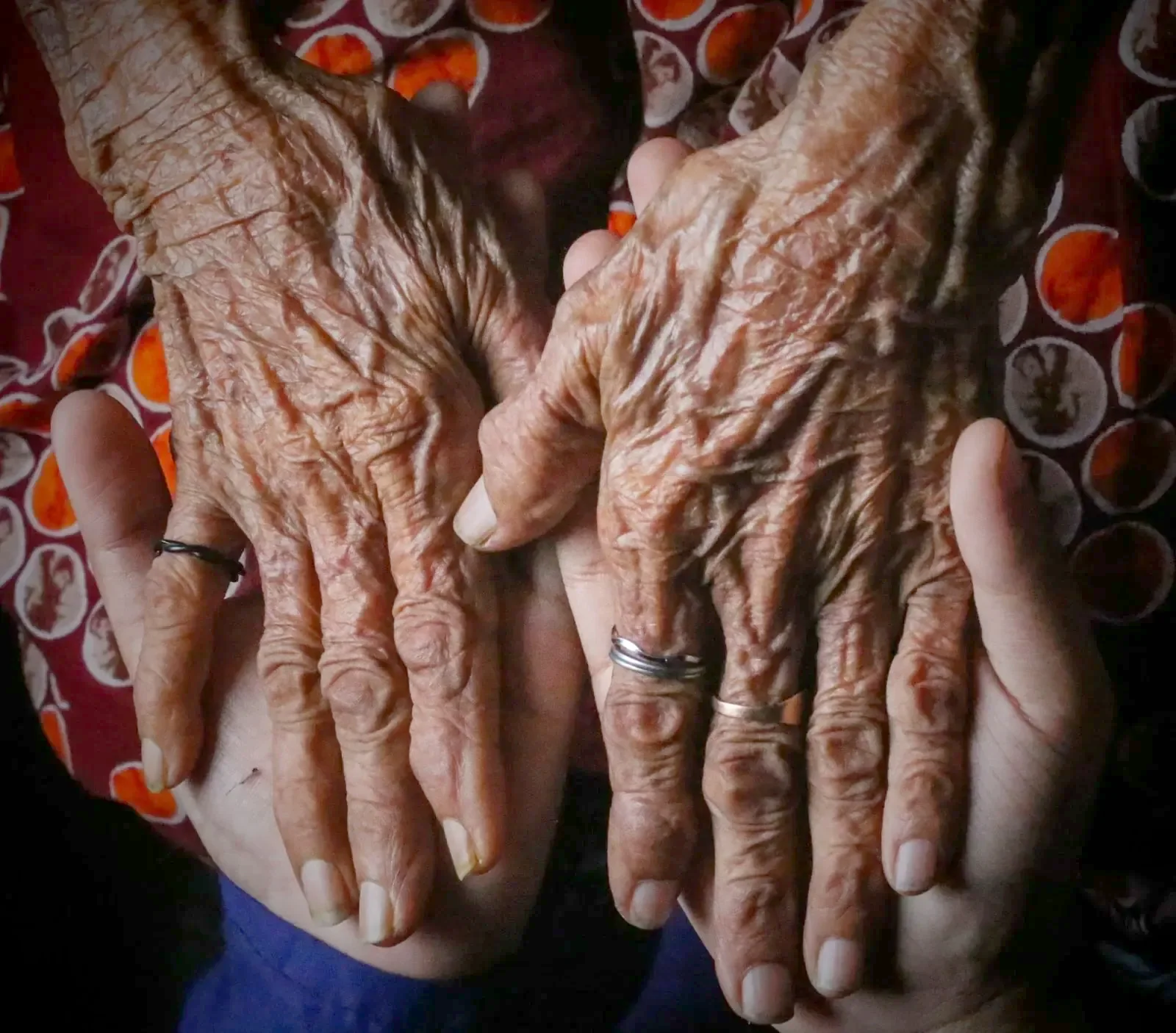 An elder&rsquo;s weathered hands resting in a younger person&rsquo;s hands