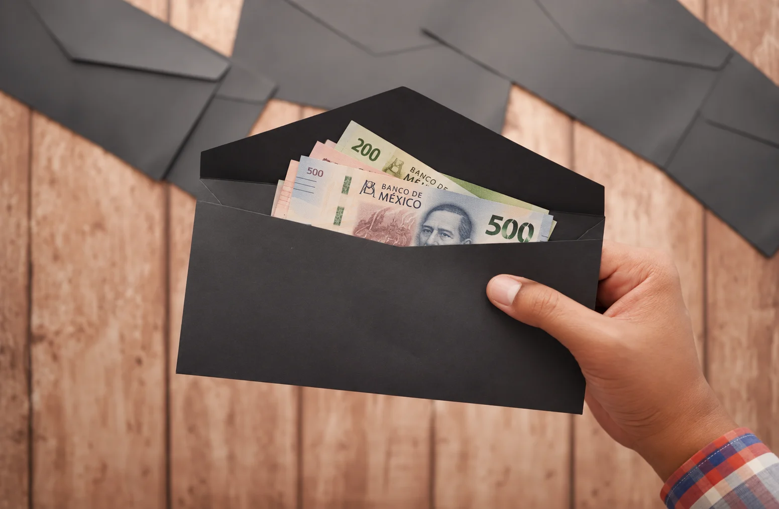 A hand holding a black envelope of Mexican peso bills